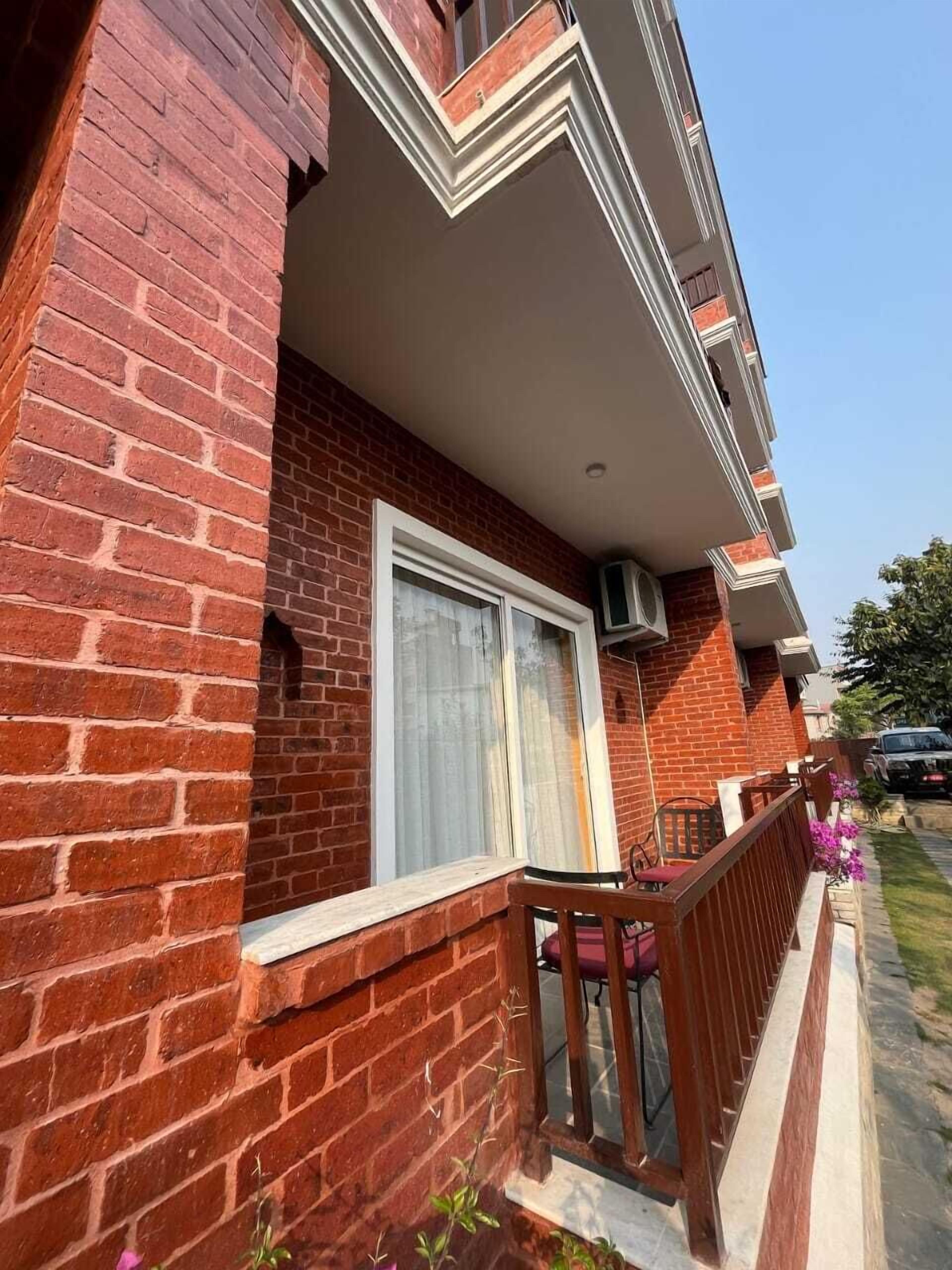 A brick building with a balcony, a window with curtains, and a small outdoor seating area.