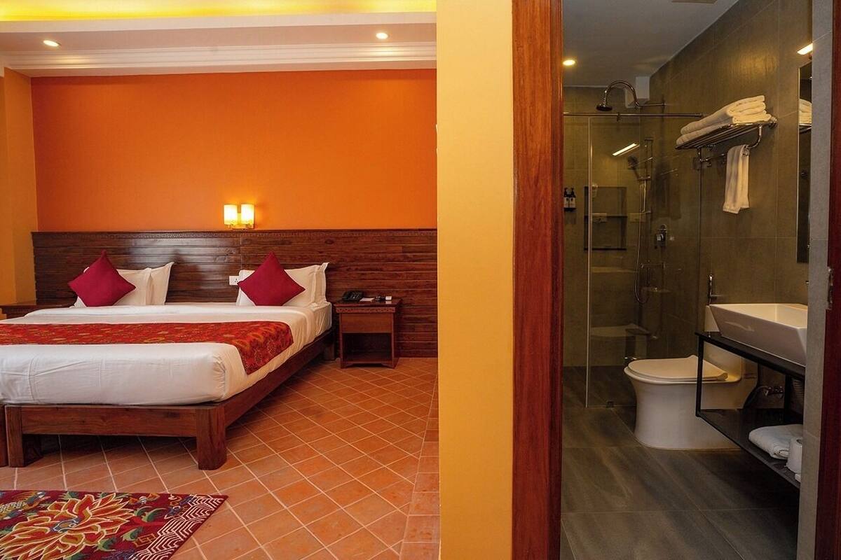 A hotel room with a wooden bed, red pillows, a bedside table, a glass shower enclosure, and a white sink.