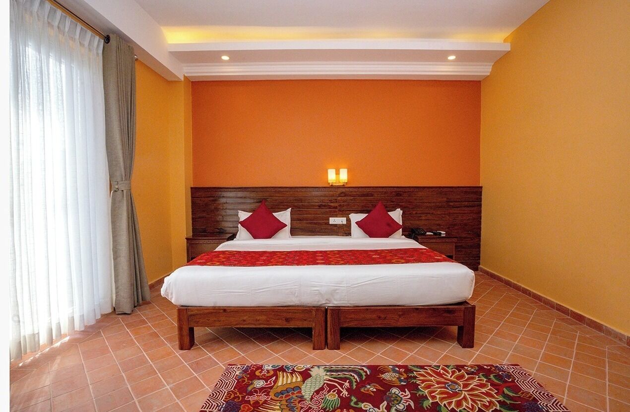 A hotel room with a wooden headboard, two red pillows, a white bedspread, and a patterned rug on the floor.