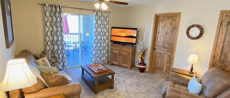 A living room with a sofa, armchair, coffee table, TV, and a sliding glass door leading to an outdoor area.