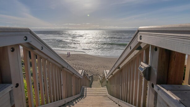 A wooden staircase leading to a beach with a clear view of the ocean. - Wandering Star (Depoe Bay)