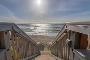 Un escalier en bois mène à une plage d’où l’on a une vue dégagée sur l’océan.