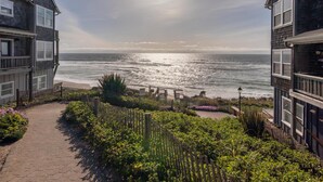 A coastal view from a building with a paved walkway leading to a wooden deck overlooking the ocean. - Wandering Star (Depoe Bay)