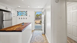 Eine Küche mit weißen Schränken, einer Holzausziehtafel, einem Edelstahlkühlschrank und einem Fenster mit Blick auf Palmen.