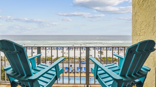 Un balcon avec deux fauteuils Adirondack bleus donnant sur une plage, une piscine et des parasols de plage.