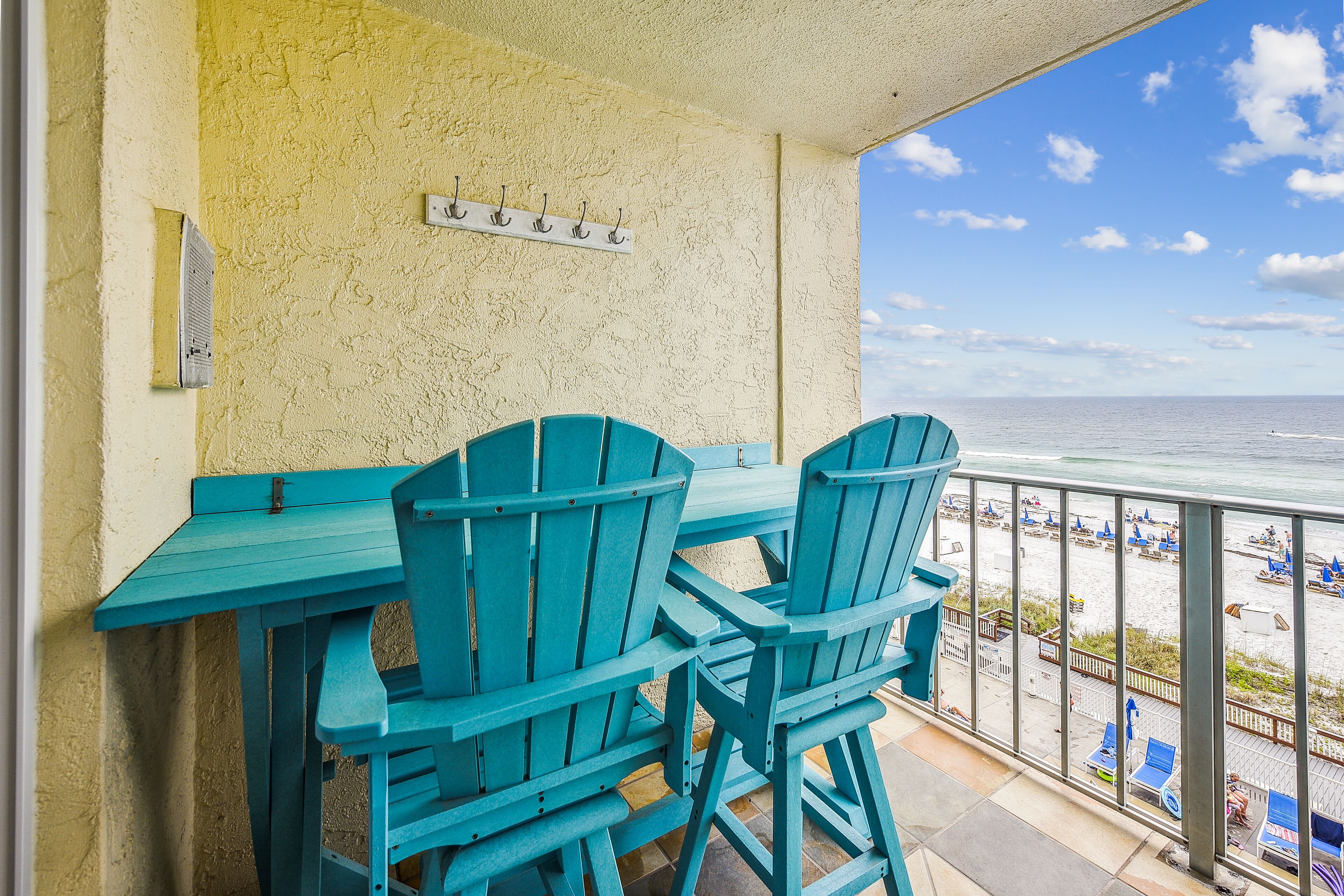 A balcony with a table and chairs, overlooking a beach with lounge chairs and umbrellas.