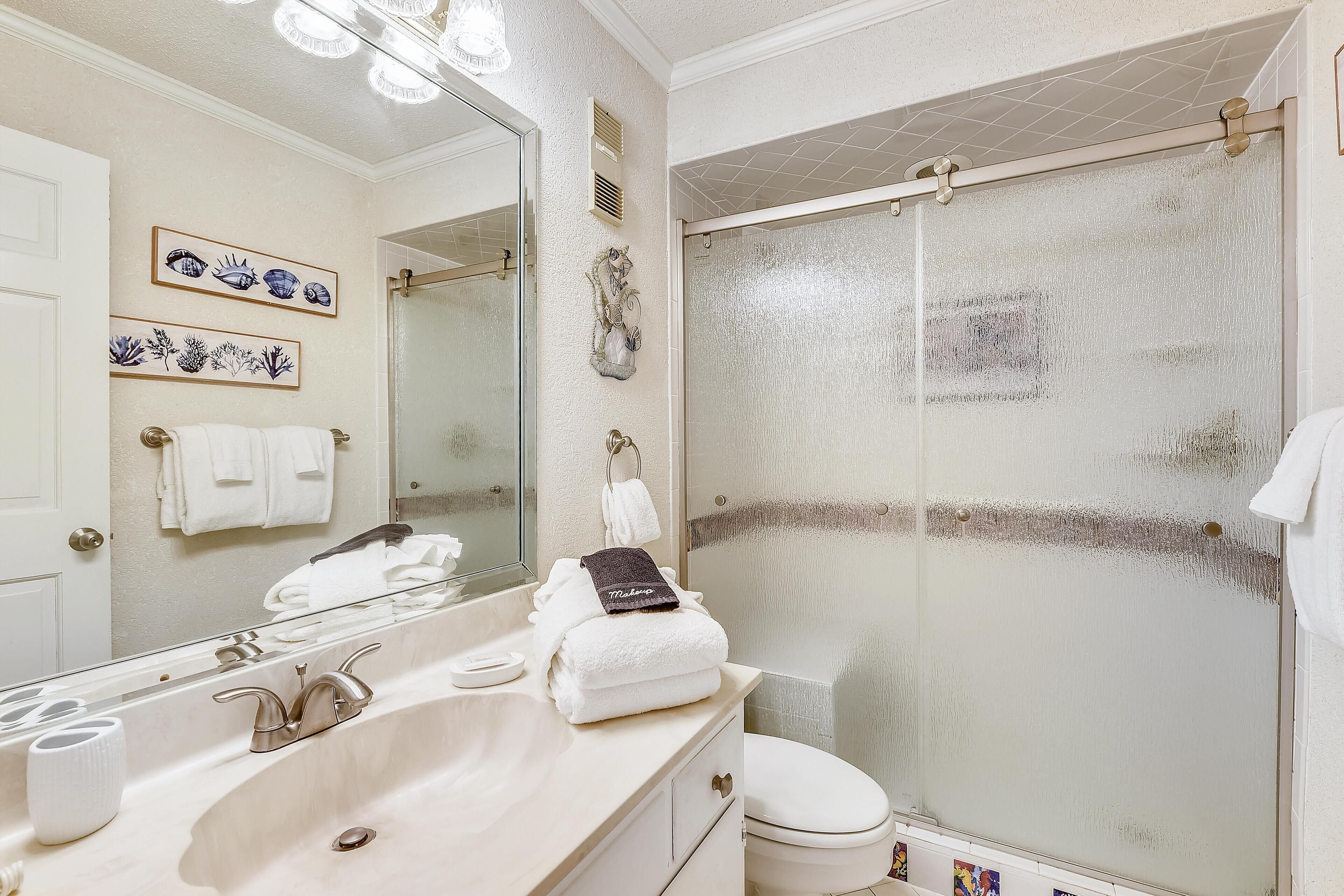 A bathroom with a large mirror, a sink, a toilet, and a shower with a glass door.