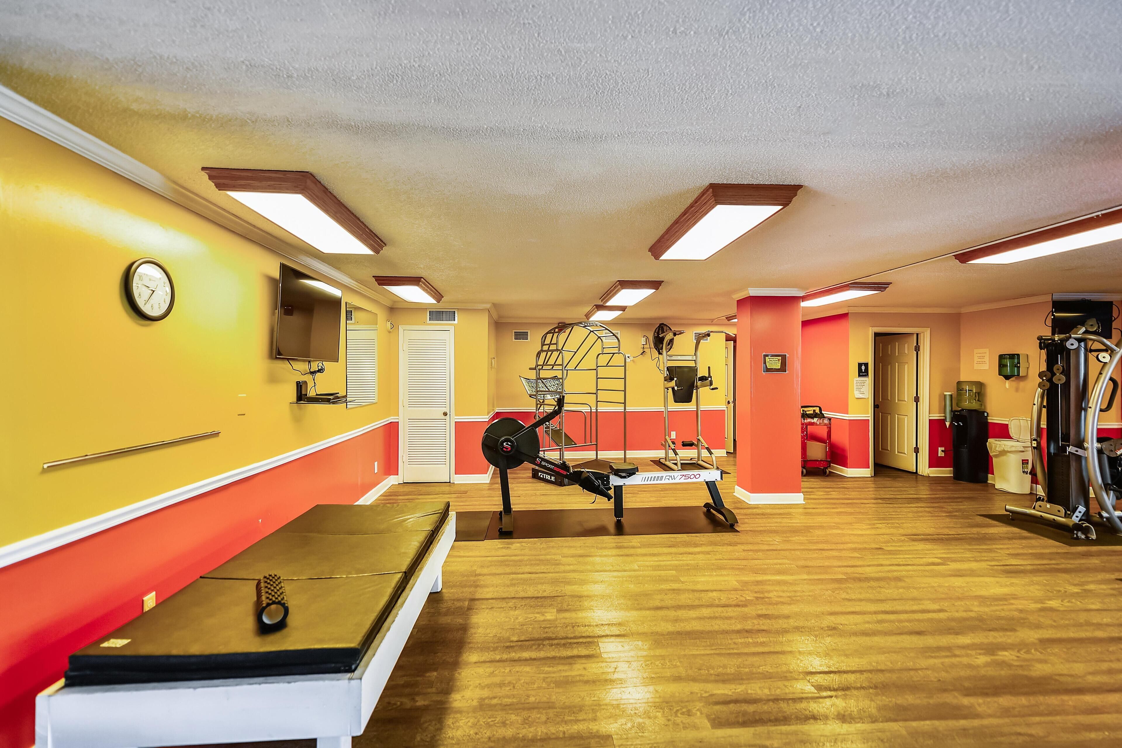 Ein Fitnessraum mit Trainingsgeräten, einer Uhr und einer Sitzbank.