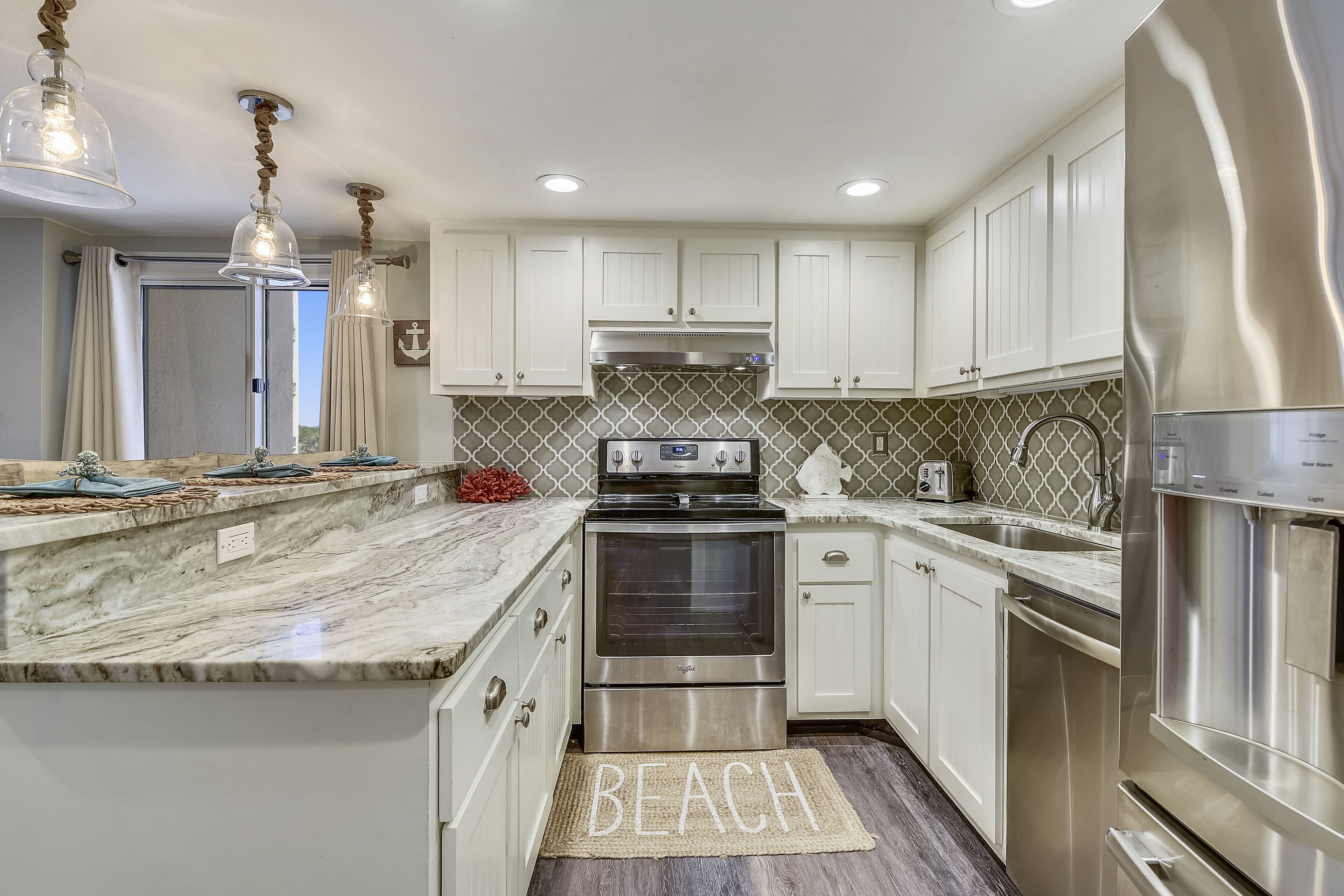 A modern kitchen with white cabinets, stainless steel appliances, and a marble countertop.