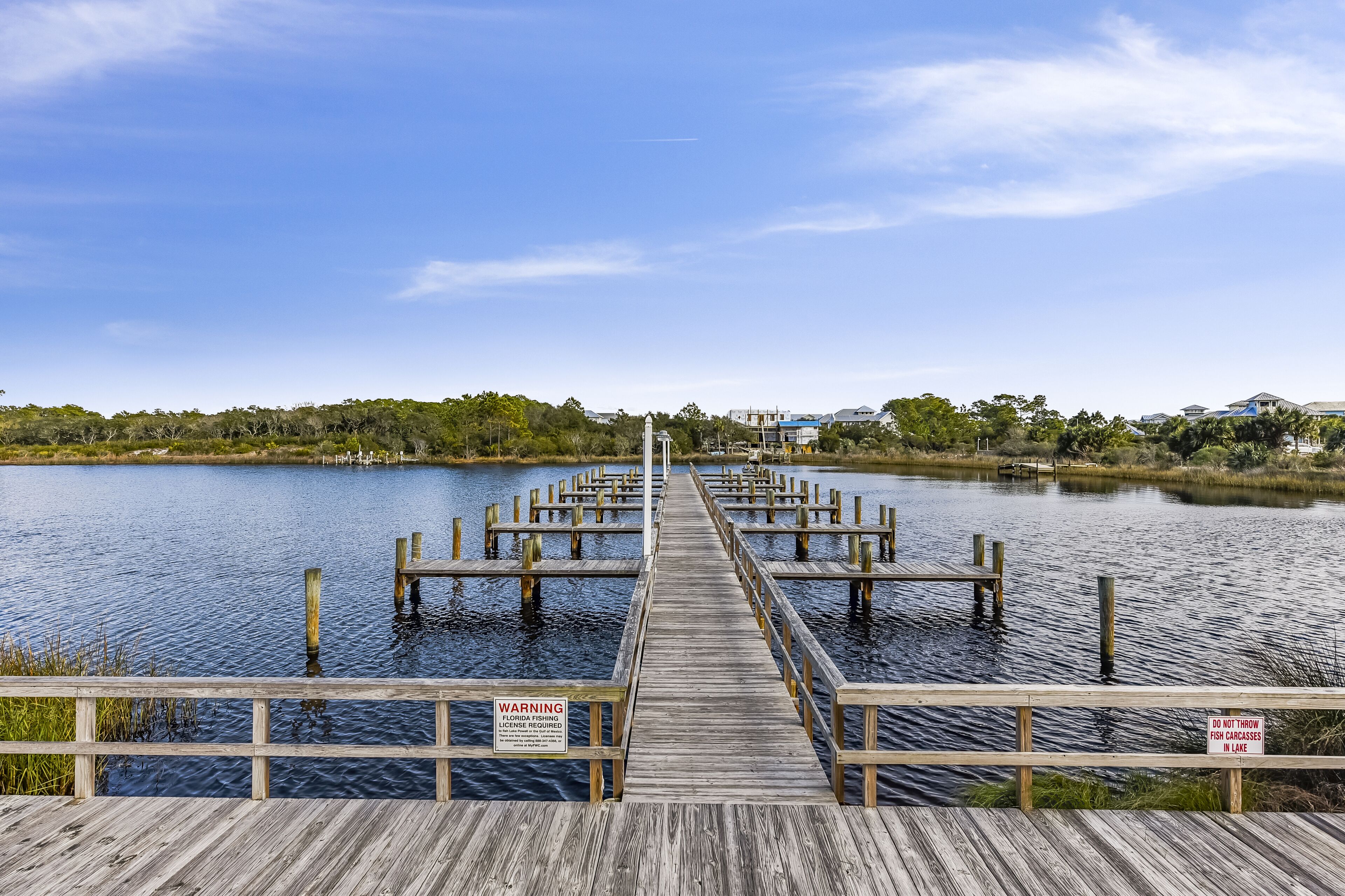 Un muelle de madera que se adentra en aguas tranquilas, con un letrero que indica la necesidad de una licencia de pesca.