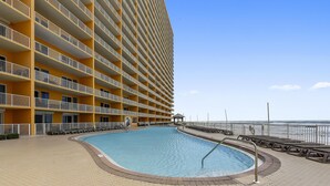 Een hotel met een zwembad, uitzicht op het strand en een hoog gebouw met balkons.