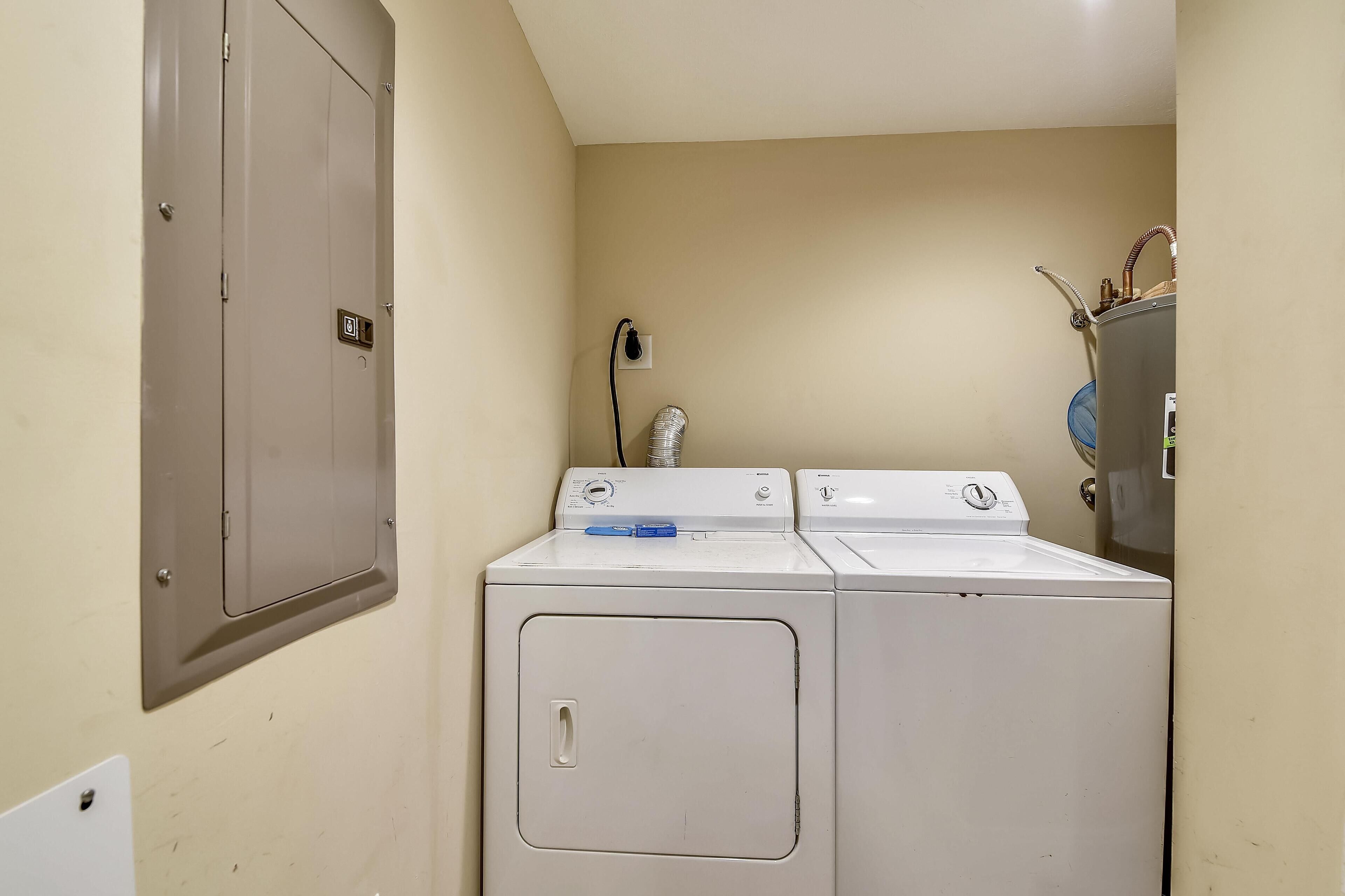 A laundry room with two stacked washers and dryers, a water heater, and a door with a lock.