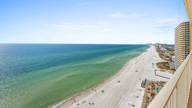 Een strand met helder turquoise water, een zandstrand en een hoog gebouw aan de rechterkant.