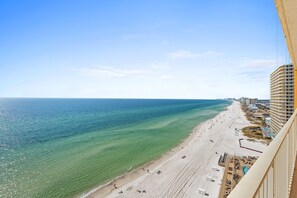 A beach with clear turquoise water, a sandy shore, and a high-rise building on the right. - Treasure Island by Book That Condo (Panama City Beach)