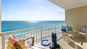 A balcony with a view of the ocean, a striped towel, a blue water bottle, and a lounge chair. - Emerald Beach by Book That Condo (Panama City Beach)