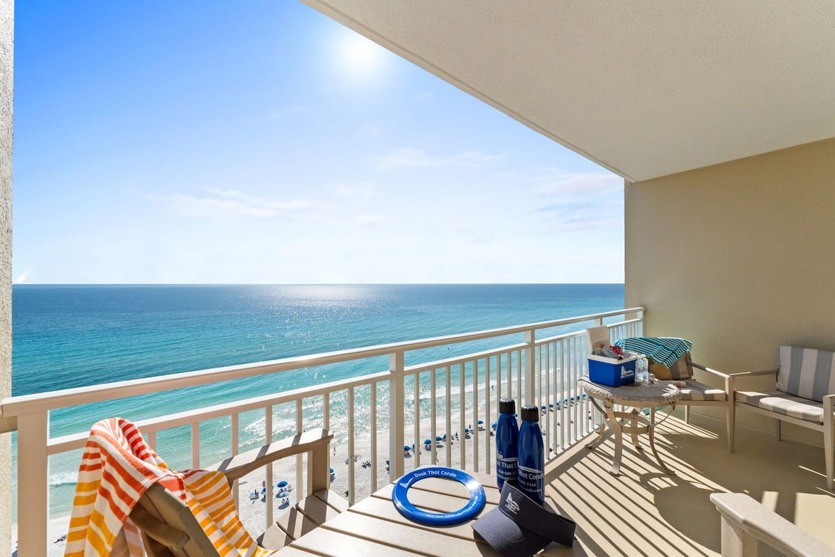 Ein Balkon mit Blick auf das Meer, ein gestreiftes Handtuch, eine blaue Wasserflasche und eine Liege.
