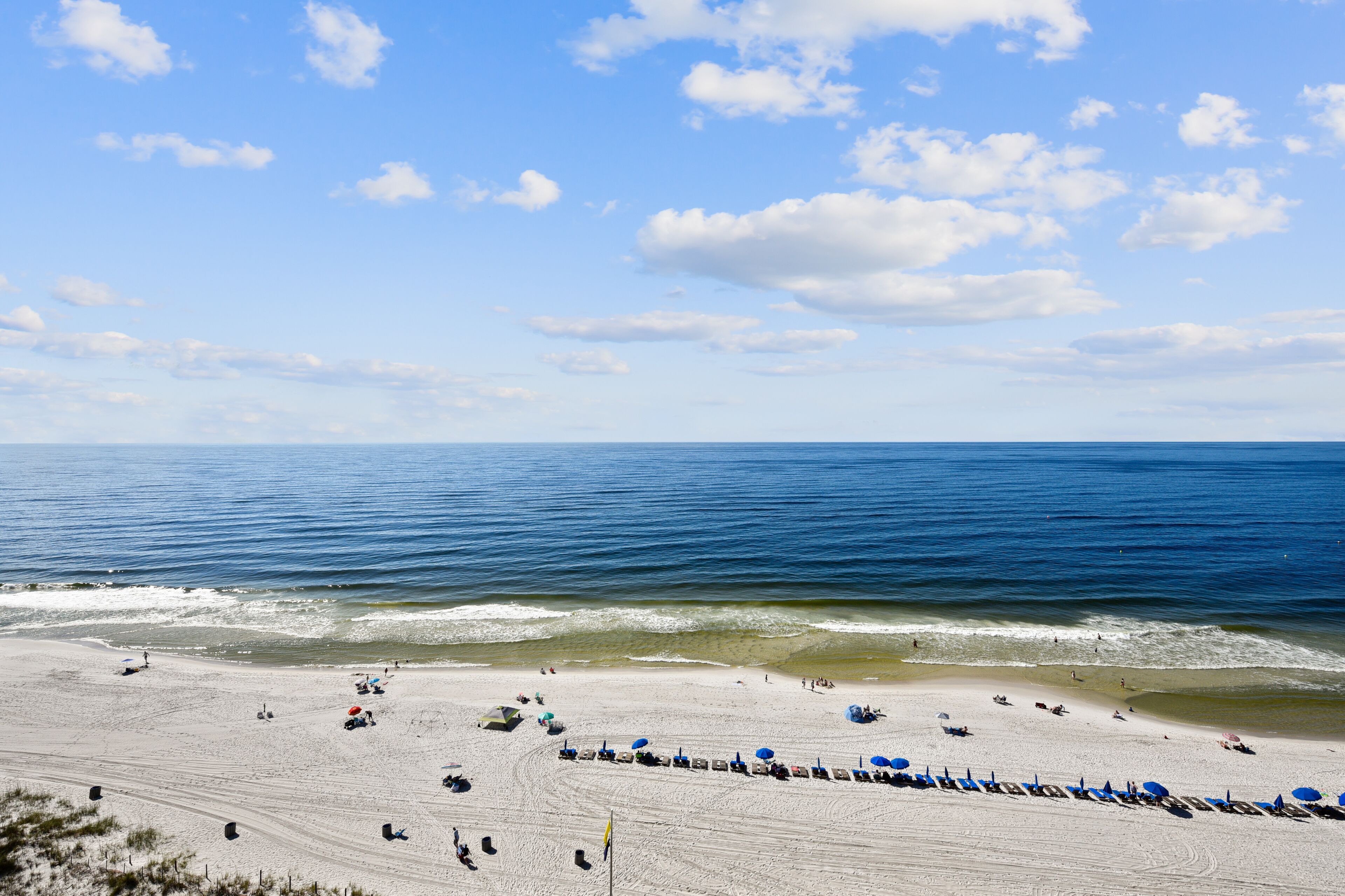 A beach with a sandy shore, a flag, and a clear blue sky.