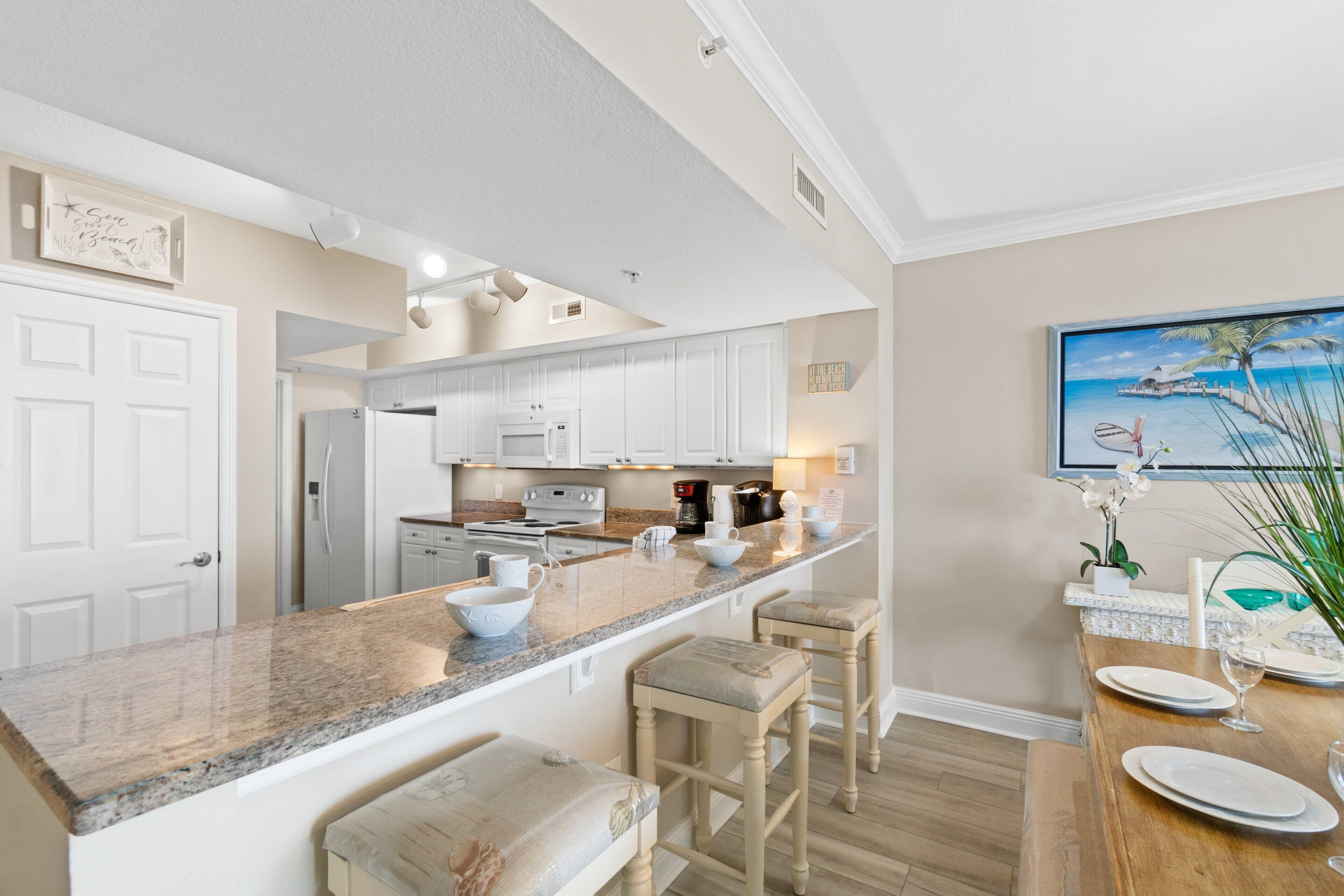A modern kitchen with white cabinets, a granite countertop, and a dining area with a wooden table and bar stools.
