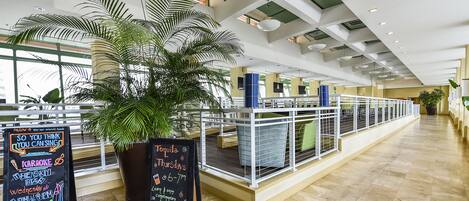 Een ruime binnenzone met een hoge plafond, potplanten en een lange balie met een balustrade.