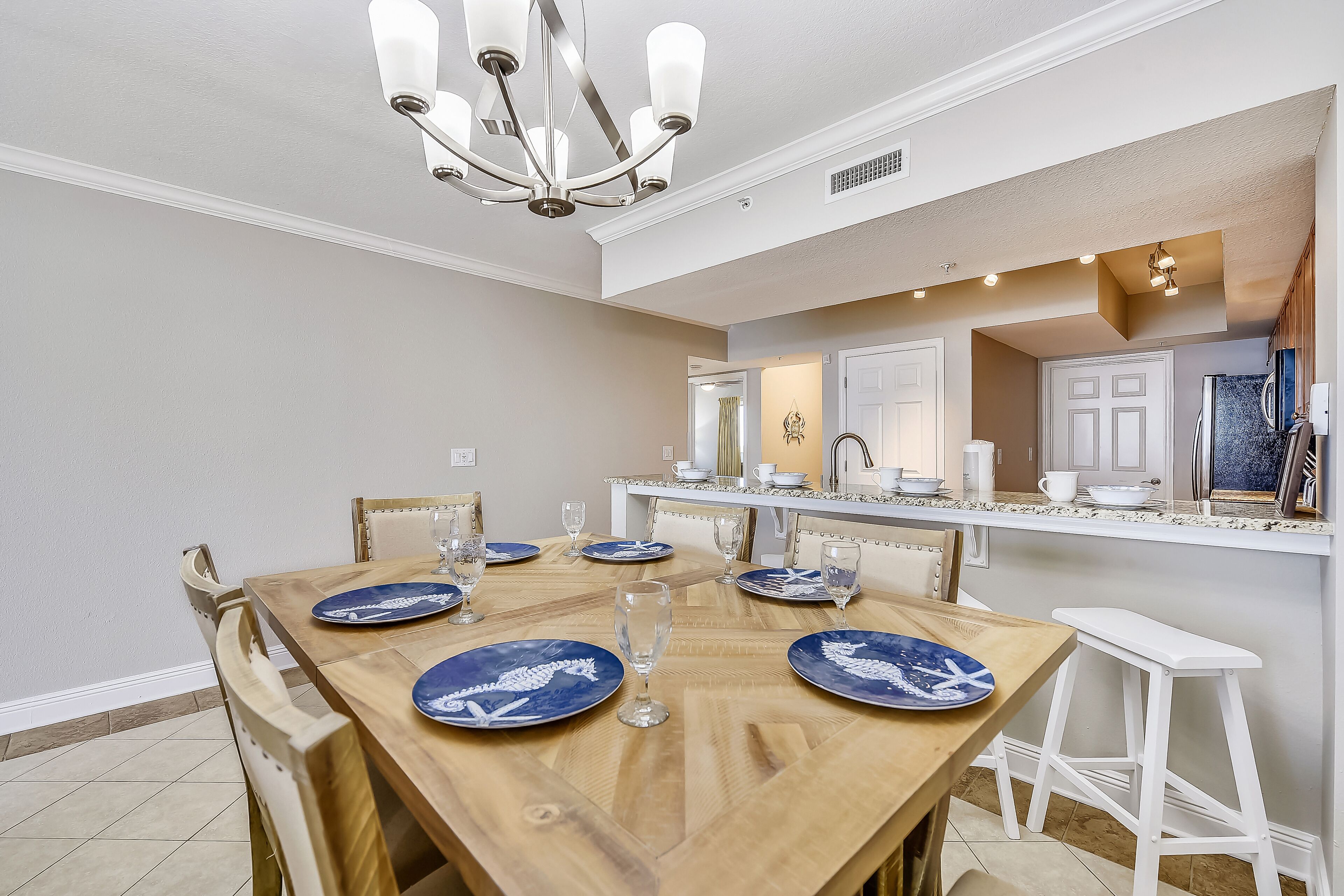 A dining area with a wooden table set for six, white chairs, and a white bar stool.