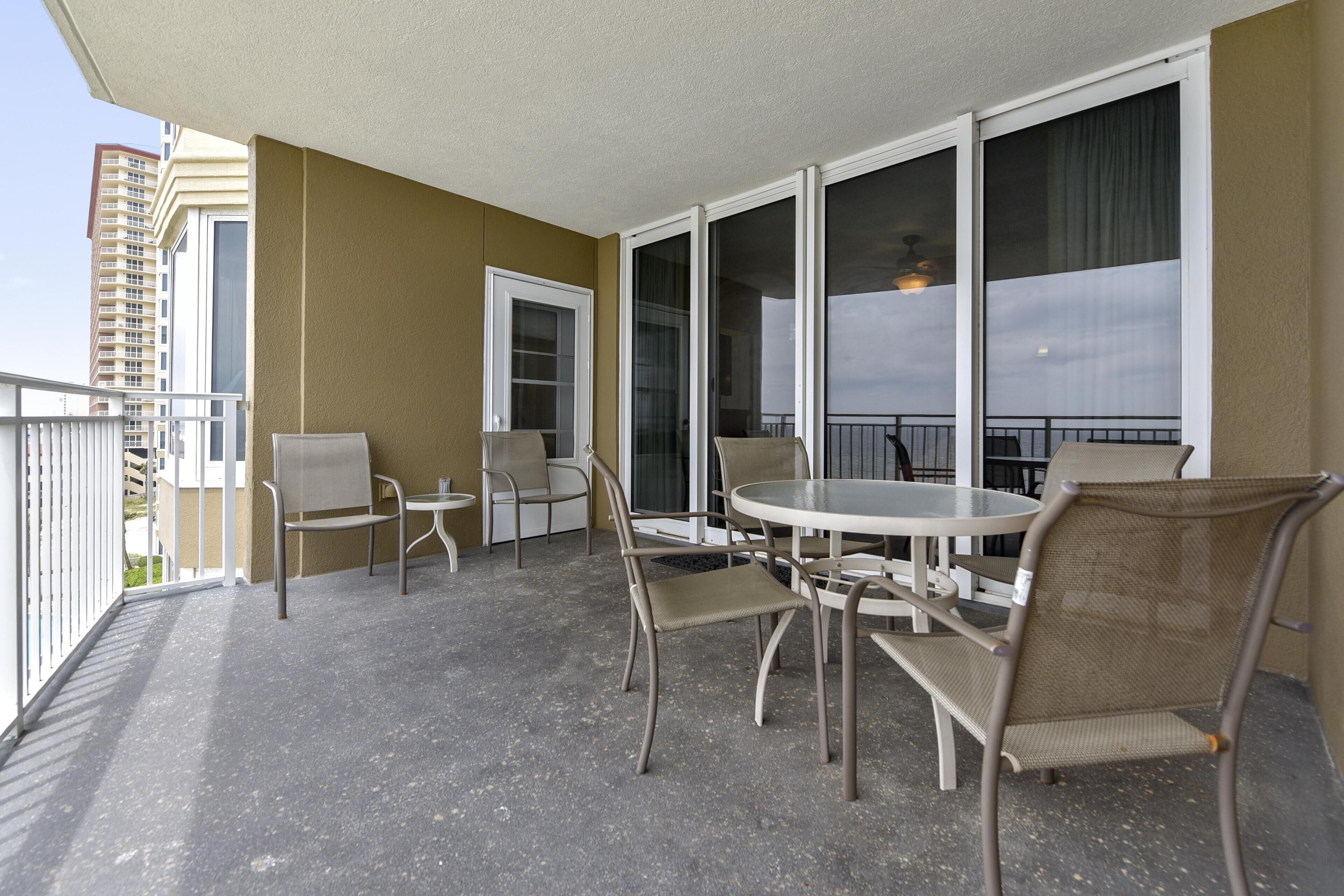 A balcony with a table and chairs, a door, and large windows.