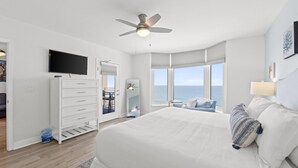 A bedroom with a large bed, a ceiling fan, a TV, and a view of the ocean. - Emerald Beach by Book That Condo (Panama City Beach)