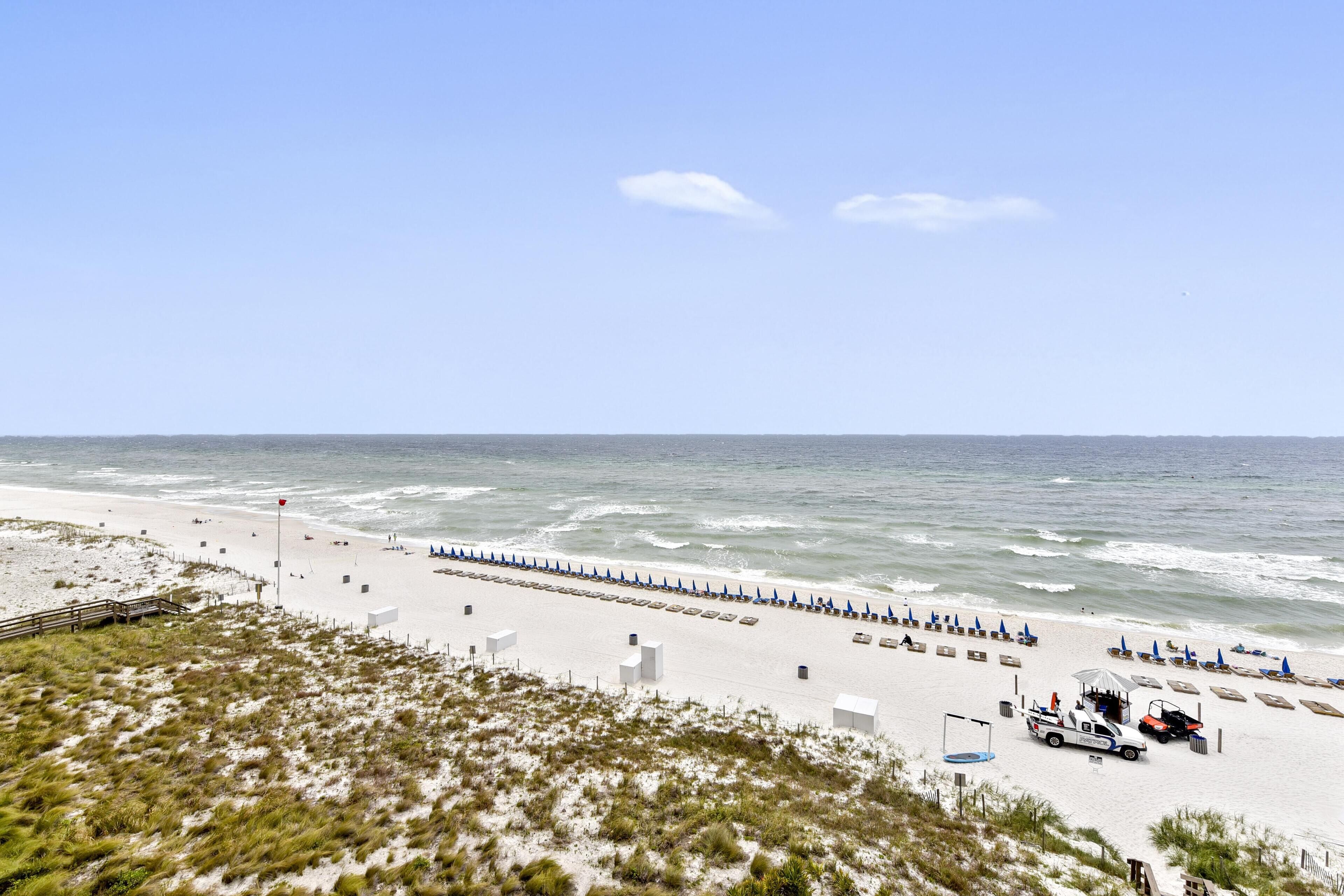 A beach with a wooden walkway, beach umbrellas, and a lifeguard tower.
