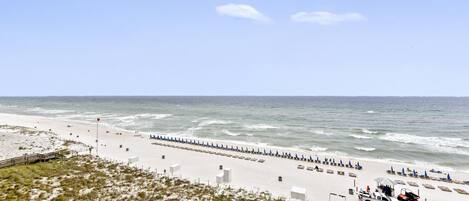 A beach with a wooden walkway, beach umbrellas, and a lifeguard tower.
