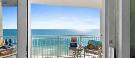 A balcony with a view of the ocean, a chair, a small table, and a cooler.