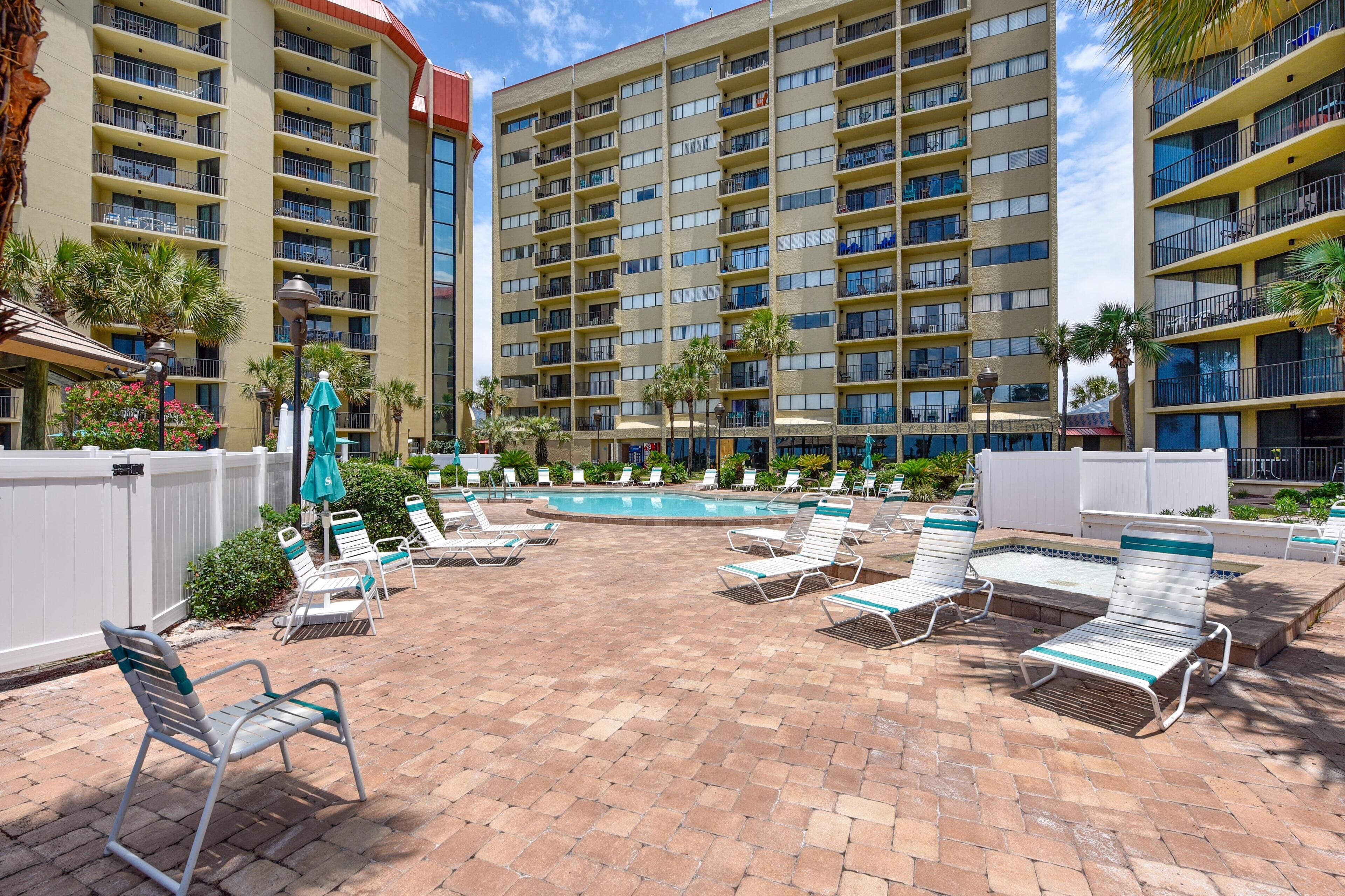 A hotel courtyard with a swimming pool, lounge chairs, and a white fence.
