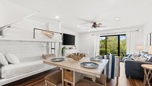 A modern, well-lit room with a bunk bed, a dining table with chairs, a sofa, and a TV. - Beachwalk by Book That Condo (Panama City Beach)