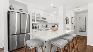A modern kitchen with a stainless steel refrigerator, white cabinetry, and a central island with bar stools. - Beachwalk by Book That Condo (Panama City Beach)