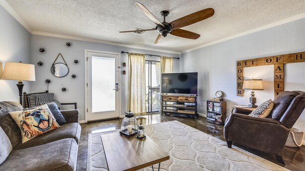 A living room with a ceiling fan, a sofa with a tiger-themed pillow, a coffee table, and a TV. - Beachwalk by Book That Condo (Panama City Beach)