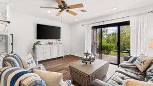 A modern living room with a flat-screen TV, a ceiling fan, and a large sliding glass door leading to an outdoor area. - Beachwalk by Book That Condo (Panama City Beach)