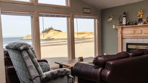 Una sala de estar con vista a la playa, una chimenea y un ventanal grande.
