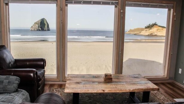 Una habitación con un ventanal grande con vistas a la playa, un sofá de cuero y una mesa de madera con un objeto decorativo.