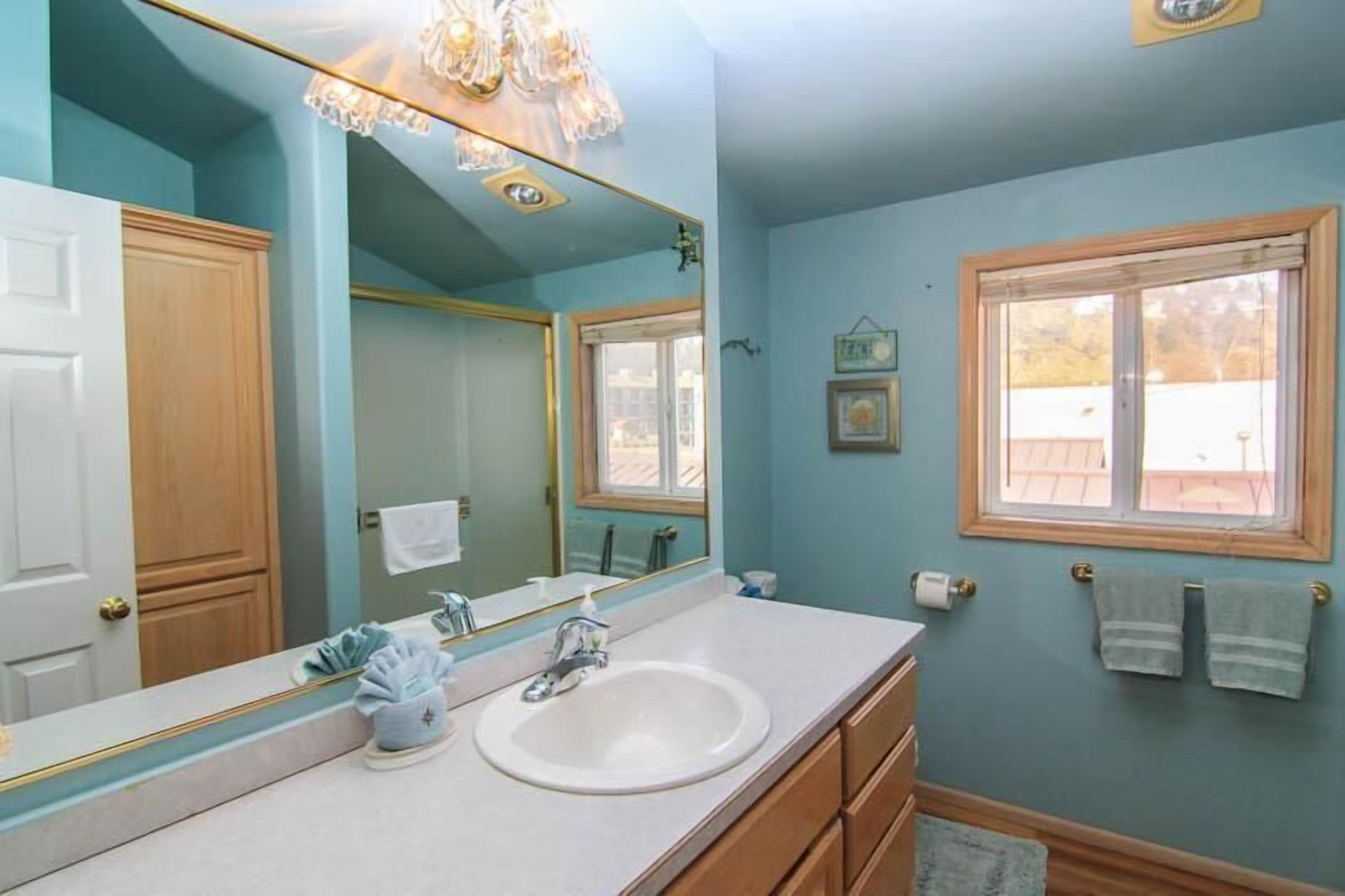 A bathroom with a white sink, a large mirror, and a window with a wooden frame.