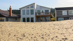 Una casa moderna de dos pisos con balcón, situada en una playa arenosa.