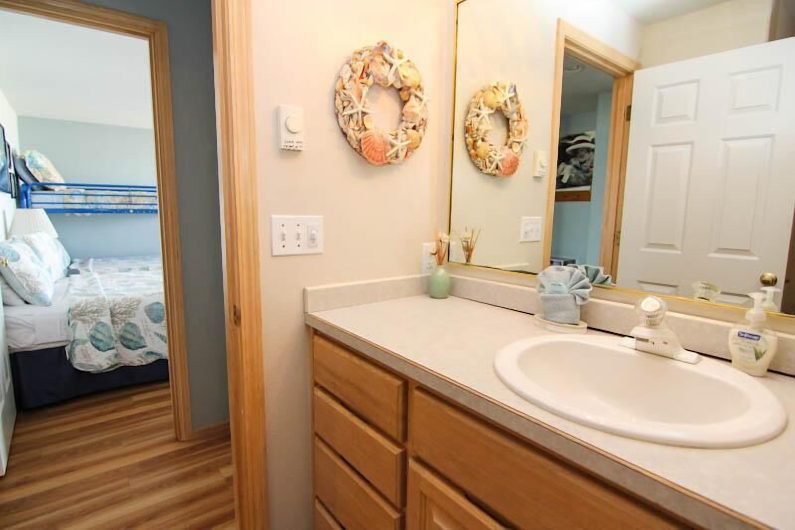 A bedroom with a bunk bed, a bathroom with a sink, mirror, and decorative wreaths.
