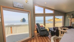 Una habitación con piso de madera, un ventanal con vista a la playa, un sillón de cuero negro y una mesa de madera.