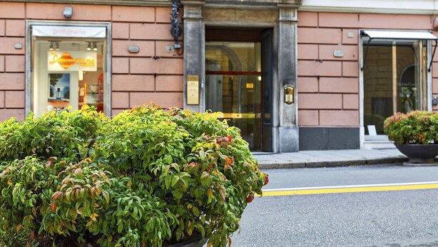 A building with a red brick facade, a glass entrance, and a small garden in front. - Via Roma Luxury Apartment (Genova)