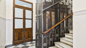 A staircase with a metal railing and a wooden handrail, leading to a door with glass panels. - Via Roma Luxury Apartment (Genova)