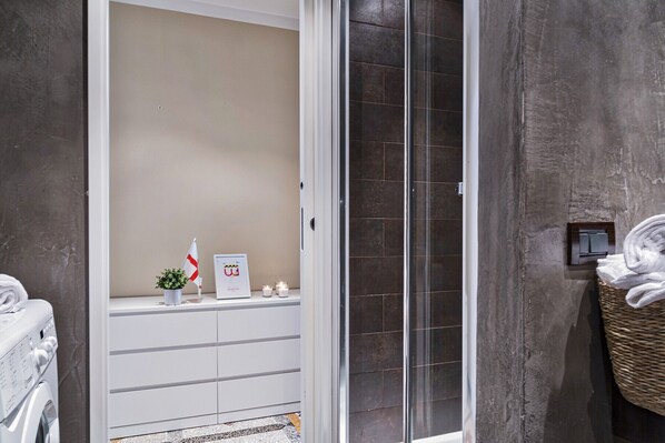 A modern bathroom with a glass shower enclosure, a white cabinet with toiletries, and a wicker basket with towels.
