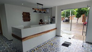 A reception area with a white counter, a wooden accent, and a modern pendant light fixture. - Hotel Jar8 (Veracruz)