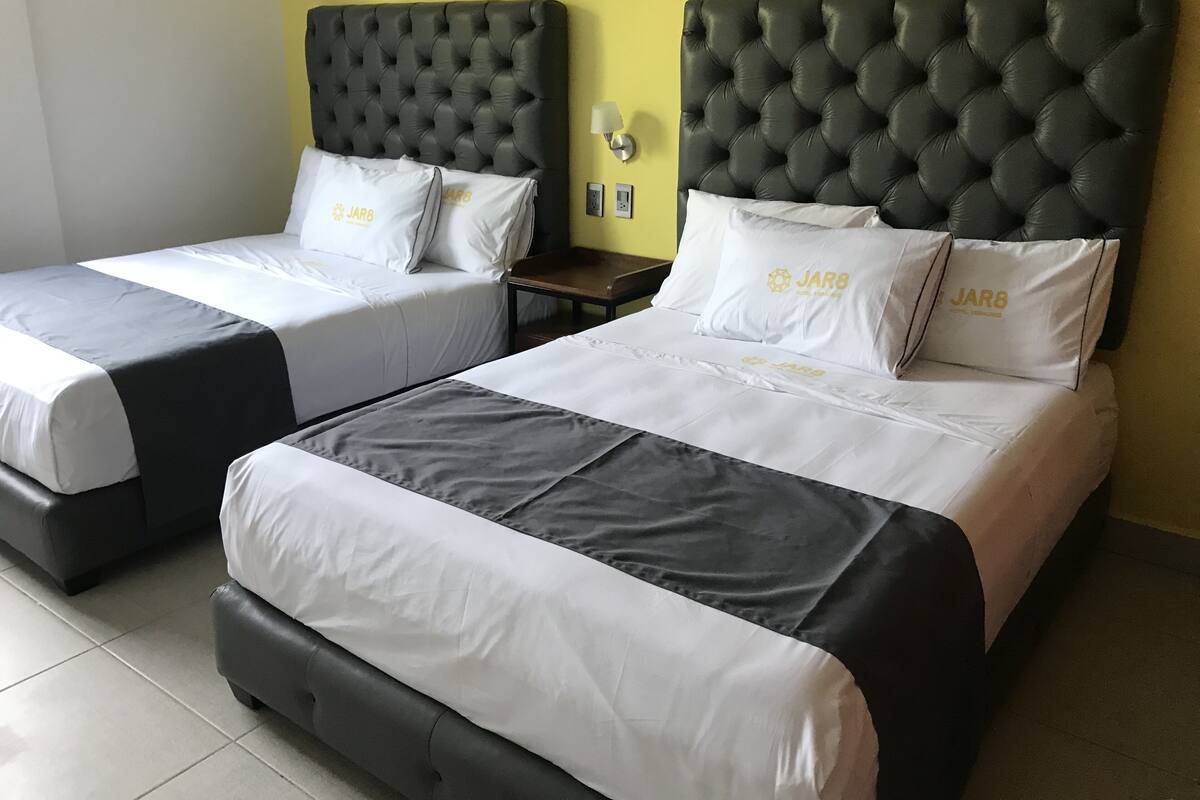 Two twin beds with black headboards and white bedding, a nightstand, and a wall-mounted lamp.
