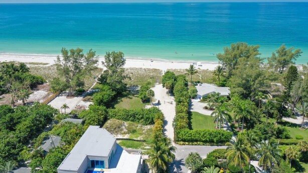 Une propriété située sur la côte, avec vue sur la plage, entourée d’une végétation luxuriante et de palmiers.