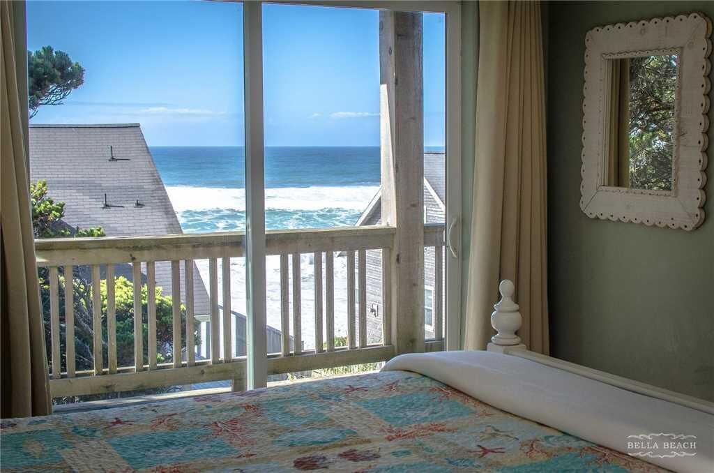 A bedroom with a large window overlooking the ocean, a wooden deck, and a bed with a floral bedspread.