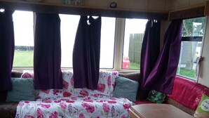 Un intérieur chaleureux avec un canapé-lit recouvert d’un tissu à motifs floraux, un banc en bois et des rideaux violets.