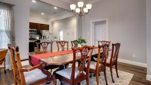 A dining room with a wooden table and chairs, a chandelier, and a view into the kitchen.