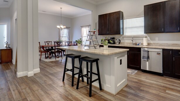 A modern kitchen with dark wooden cabinets, a central island with bar stools, and a dining area with a chandelier.